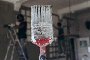 Detailed close-up of a paintbrush with men painting a wall in the blurred background, highlighting renovation work.